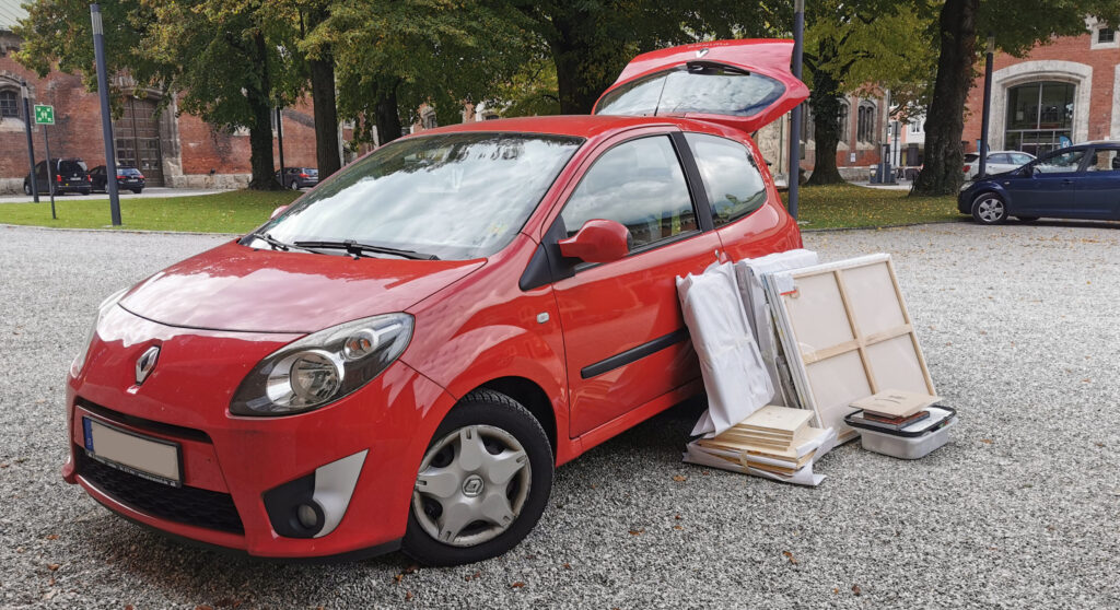 Ein rotes Auto wir mit Bildern beladen, um sie in eine Ausstellung transportieren