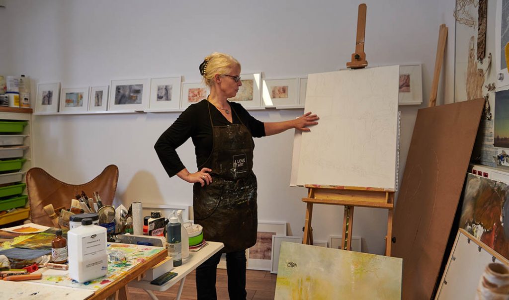 Künstlerin im Atelier vor weißer Leinwand, nach Inspiration suchend
